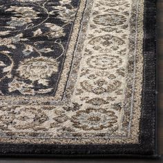 a black and white area rug with an ornate design on the bottom, in front of a wooden floor