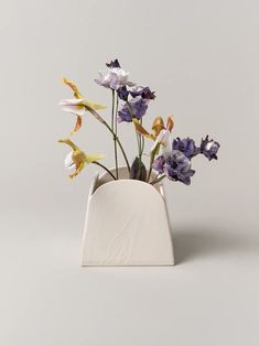 a white vase with purple and yellow flowers in it