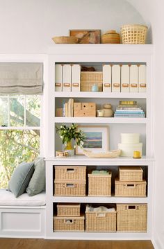 a white bookcase filled with lots of books and wicker baskets next to a window