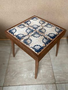 a wooden table with blue and white tiles on it's top, sitting in front of a beige wall