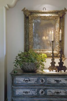 an ornate dresser with two candles on top and a potted plant next to it