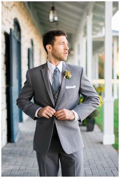 a man in a suit and tie standing on a porch with his hands in his pockets