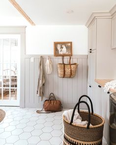 a laundry room with white walls and flooring has baskets hanging on the wall next to an ironing board