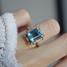 a woman's hand holding a ring with an aqua blue topazte surrounded by filigrees