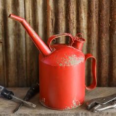 an old red tea pot with a pipe on it and tools next to it in front of a corrugated wall