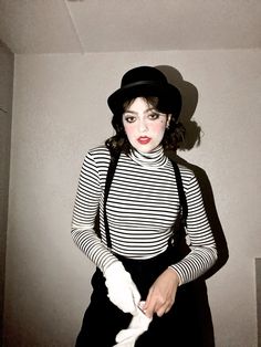 a woman in black and white striped shirt holding a pair of gloves while standing next to a wall