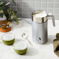 a coffee maker sitting on top of a counter next to two cups and a spoon