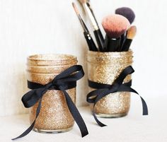 two jars filled with makeup brushes on top of a table