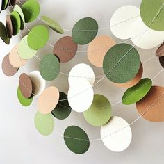 some paper circles hanging from a string on a white wall with green and brown leaves