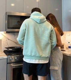 a man and woman standing in front of an oven looking at something on the counter