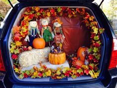 the back of a car with pumpkins, hay and scarecrows in it