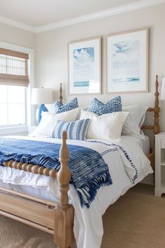 a bed with blue and white pillows in a bedroom next to two framed pictures on the wall