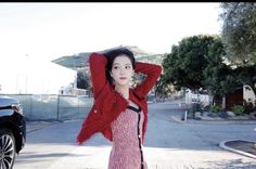 a woman is standing on the street with her arms behind her head and wearing a red cardigan