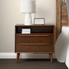 a nightstand with a clock on it next to a bed