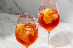 two wine glasses filled with orange slices on a marble counter top next to each other