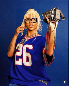 a woman with glasses holding a hair dryer in one hand and an object in the other