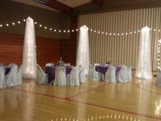 an indoor dance floor decorated with white and purple linens, draping and lights