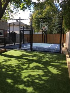 an outdoor basketball court surrounded by grass and fenced in area next to a house