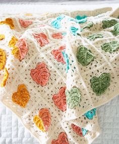 a crocheted blanket with hearts on it sitting on a white bedding sheet