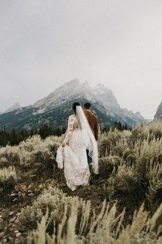 a bride and groom walking in the mountains