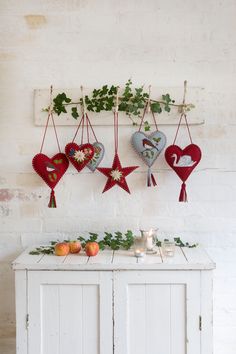 three heart shaped ornaments hanging on a wall next to a white cabinet with candles and greenery