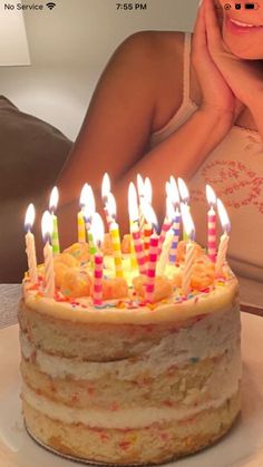 a woman sitting in front of a birthday cake with candles on it and her hand under her chin