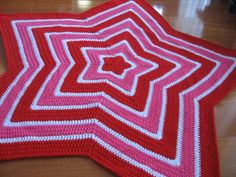 a red and white crocheted rug on top of a wooden floor in the shape of a star