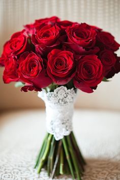 a bouquet of red roses sitting on top of a white lace covered table cloth in a vase