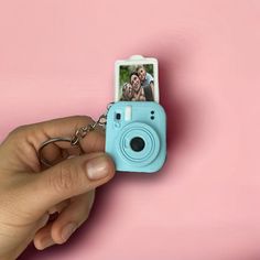 a hand holding a camera keychain with a photo attached to the front of it