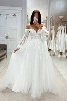 a woman taking a selfie while wearing a wedding dress in a bridal gown shop