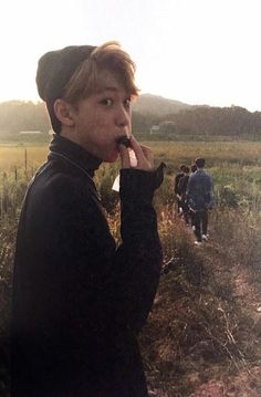 a person standing in a field with one hand on his mouth and another holding something up to their mouth