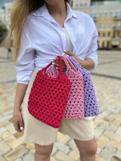 a woman holding three crocheted purses in front of her face and wearing white shirt