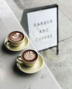 two cups of coffee sitting on top of a table next to a sign that says barber and coffee