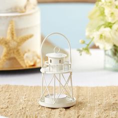 a small white lighthouse on a table with flowers in the vase behind it and a starfish figurine next to it