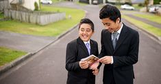 two men in suits standing on the side of a road looking at a photo album