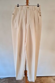 Cream drapey trousers with pleats and pocket detailing.  From Iconic Australian designer Adele Palmer this fabulous 1980's  trousers have a fixed  with wide belt loop detailing and deep front pleats.  The pocket detailing is just gorgeous with a slashed opening on the front of the body that turns back into a buttoned detail that hides the side pocket beneath.  The buttons area swirl of honey coloured beauty with the fuller leg finished with a hemmed cuff.  Seriously considered from a design poin Spring Tapered Pants With Belt Loops, Classic Tapered Pants With Belt Loops, Classic Tapered Formal Bottoms, High Waist Pleated Formal Pants, Vintage Formal Bottoms With Button Closure, Vintage Tailored Pants With Belt Loops, Retro Pleated Workwear Bottoms, Vintage Formal Bottoms With Belt Loops, Vintage Dress Pants With Belt Loops For Formal Occasions