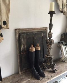 a pair of black boots sitting on top of a wooden shelf next to a candle