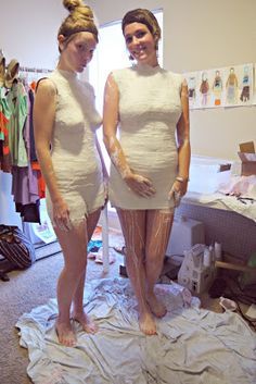 two women in white dresses standing next to each other on top of a sheet covered floor