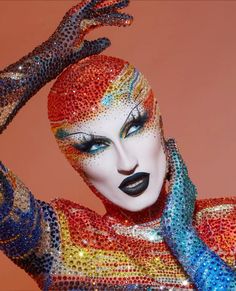 a woman with colorful makeup and body art on her face is holding her hands up to her head