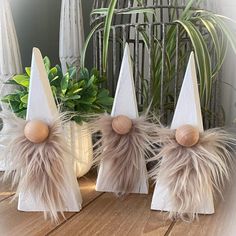 three wooden gnome hats with feathers on them sitting on a table next to a potted plant