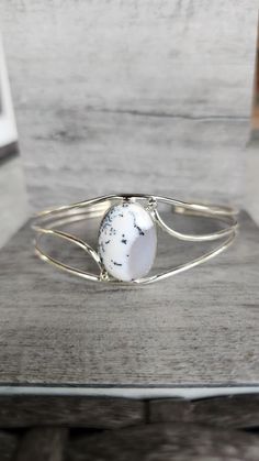 The Genuine Dendritic Opal Three Band Cuff Bracelet set in 925 Sterling Silver is a mesmerizing piece that combines natural beauty with artisan craftsmanship. Featuring a striking 1-inch high dendritic opal, known for its ethereal patterns resembling scenic landscapes, this bracelet is a unique expression of boho elegance. The handcrafted three-band sterling silver design enhances the opal's intricate details, making it a standout accessory for weddings or as a thoughtful gift. With its blend of organic charm and refined style, this bracelet is perfect for those who appreciate one-of-a-kind, handmade jewelry. Silver Opal Bracelet Gift, Dainty Adjustable Opal Bracelet, Unique Nickel-free Silver Bangle, Adjustable Hand-strung Opal Jewelry, Dendritic Opal, Silver Design, Refined Style, Wedding Boho, Handmade Wedding