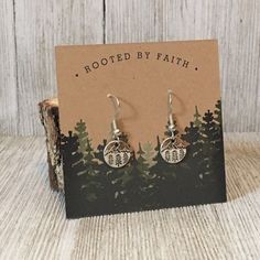 the earrings are made from metal and have pine trees on them, with words etched in it