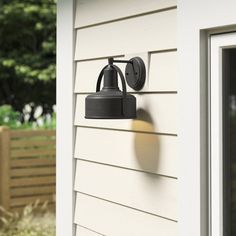 an outdoor wall light on the side of a house with trees in the back ground