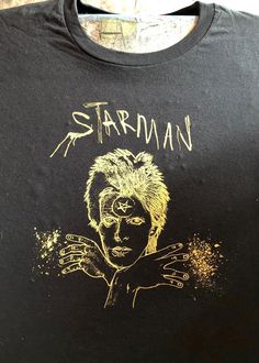 a black t - shirt with gold ink on it that says,'starman '