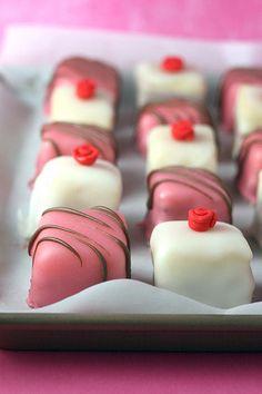 there are many pink and white desserts in the box together, with red buttons on them