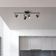 an overhead track light in a kitchen with white cabinets and black counter tops, along with stainless steel appliances