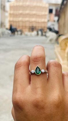 a person's hand holding a ring with an emerald and diamond in the middle