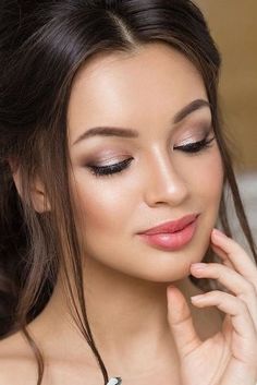 a woman with long hair and makeup looks down at the camera while holding her hand near her face