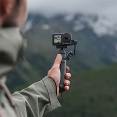 a person holding up a camera to take a photo in front of some snow covered mountains