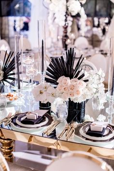 the table is set with black and white plates, silverware, and flower centerpieces